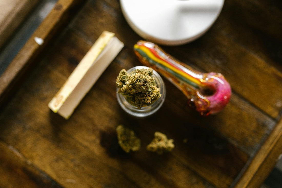 Cannabis in a small jar on a table next to a glass piece