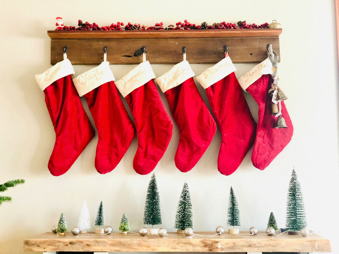 Red Christmas stockings hanging on a wooden shelf above a mantle