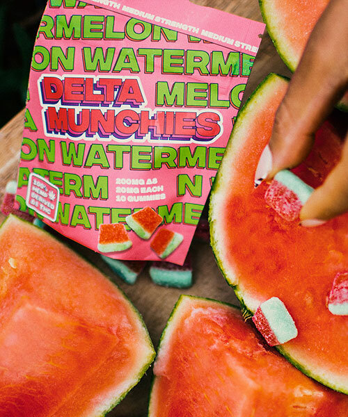 Watermelon flavored delta 8 gummies being held over a cutting board of watermelon fruit.