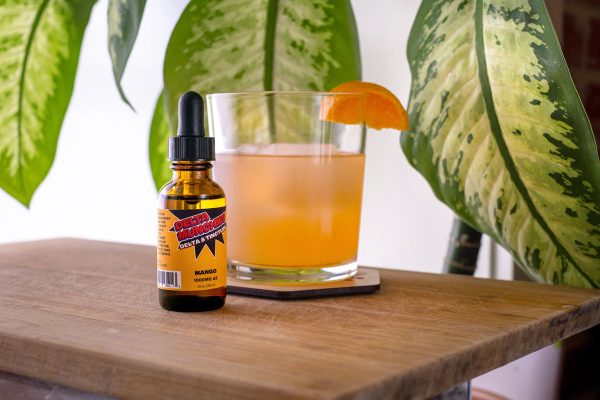 Delta 8 mango tincture resting on a table with a cocktail