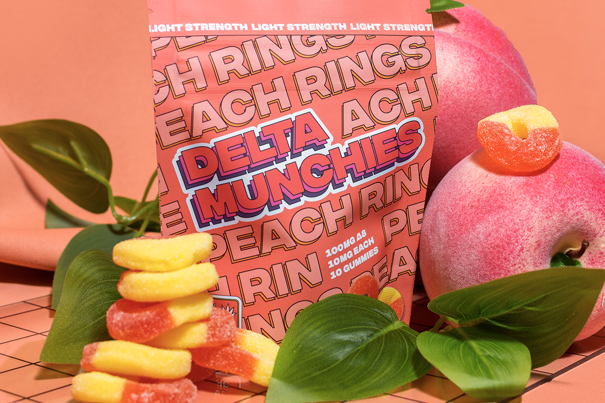 Delta Munchies Peach Ring gummies sitting next to a peach and pech tree leaves.