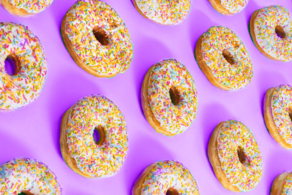 Sprinkled covered donuts on a light purple background.