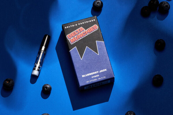 Box of Delta Munchies' Blueberry Jack delta 8 vape cartridge next to blueberries on a blue table.