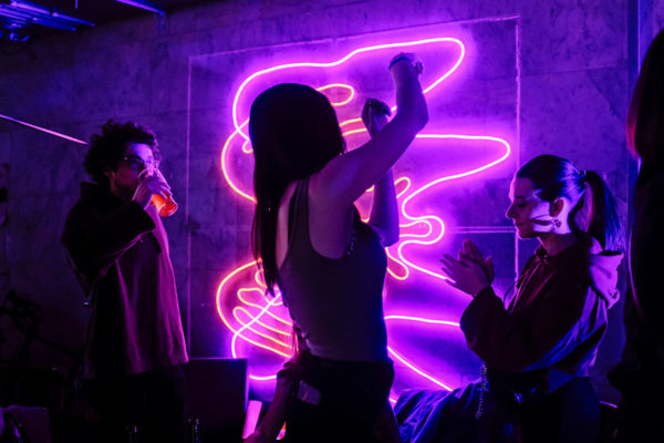 Group of people dancing and having fun in front or a purple neon sign.
