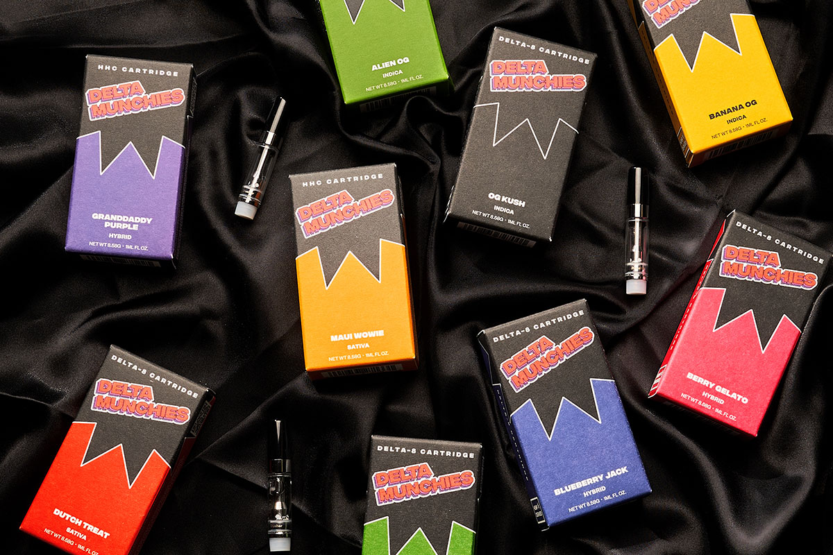 Assorted boxes of Delta Munchies' delta 8 THC vape cartridges on a rugged black fabric.