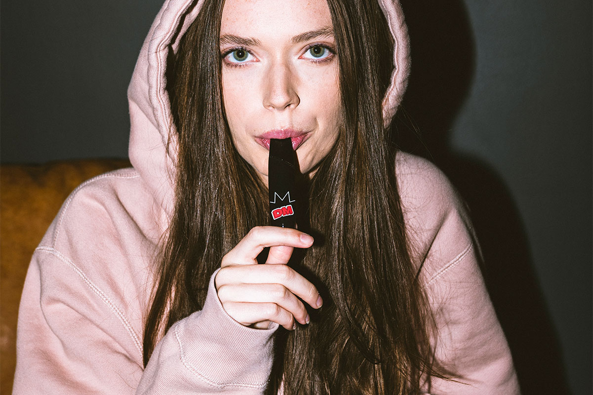 Woman with a hoodie taking a hit from a Delta Munchies disposable vape pen.