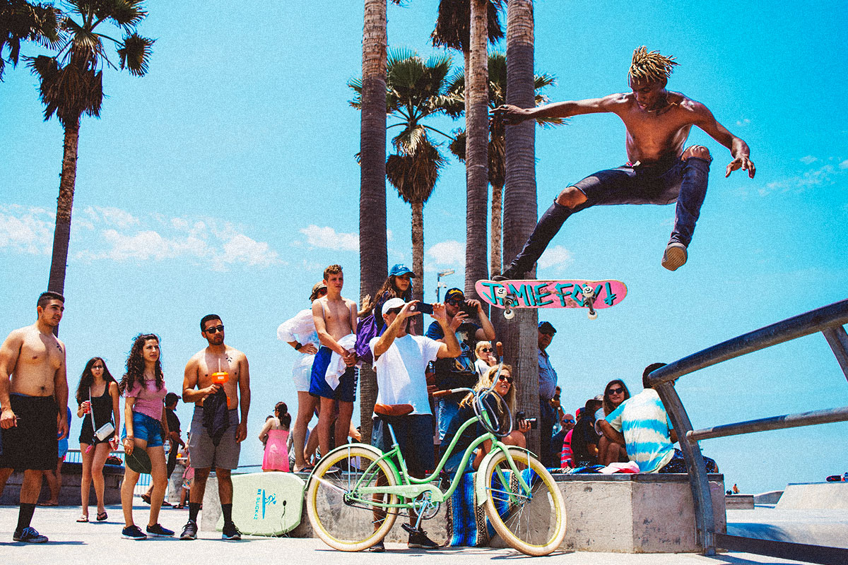 Guy performing a skate trick in front of a crowd in a California beach.