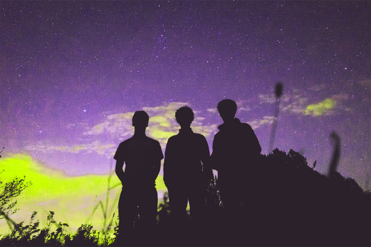 Silhouette of 3 men with a green and purple sky behind them.