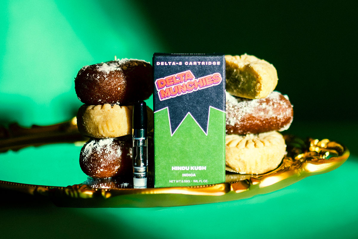 Delta Munchies' Hindu Kush Delta 8 Vape Cartridge on a golden tray next to biscuits on a green background.