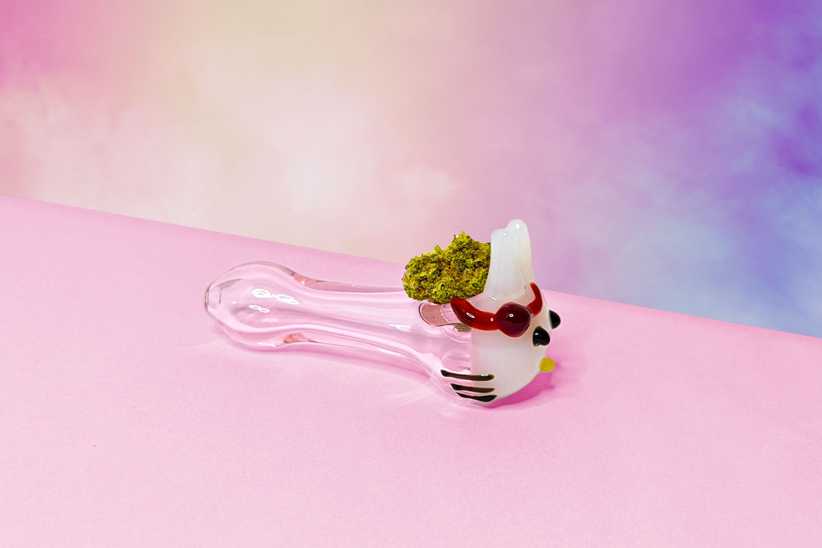 Glass pipe with a marijuana nug on a light pink table.