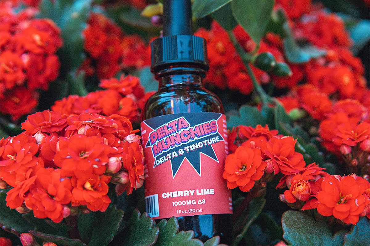 Delta Munchies' Cherry Lime delta 8 THC tincture next to red flowers.
