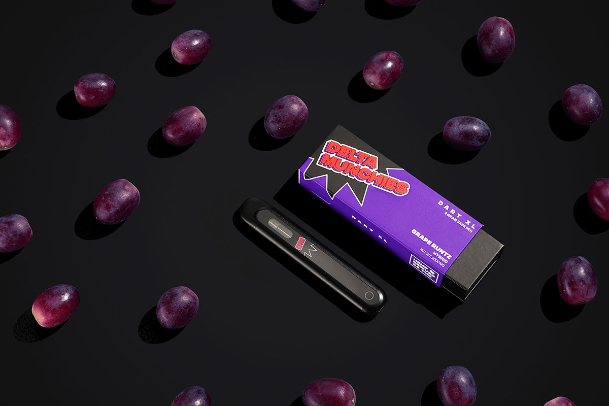 Delta Munchies' Grape Runtz Disposable Vape on a black table with grapes.