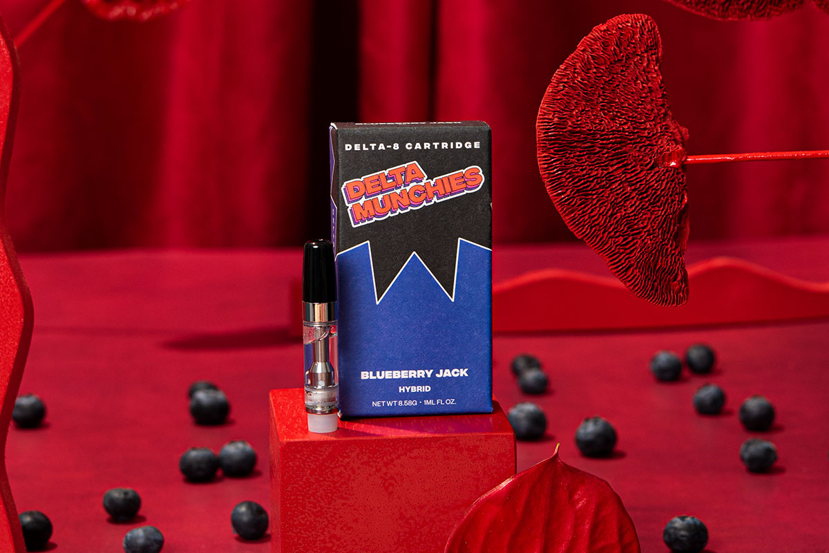 Delta Munchies' Blueberry Jack Delta 8 vape cart on a red set with blueberries on the floor.