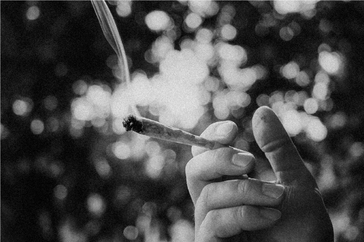A hand holding a lit joint with a black and white backdrop