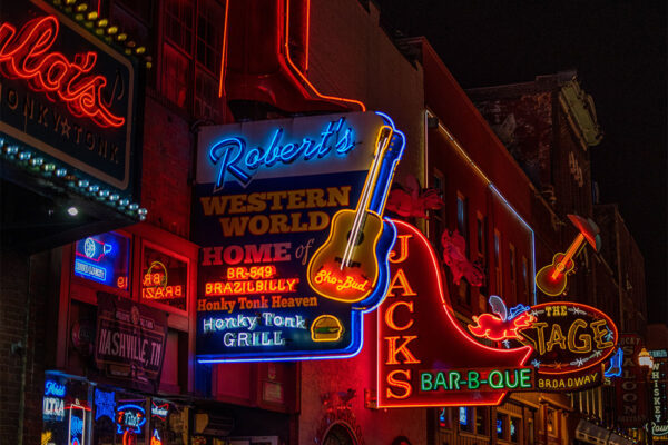 Vibrant neon lights adorn the exterior of a Nashville bar, casting a colorful glow on the bustling city street at night.