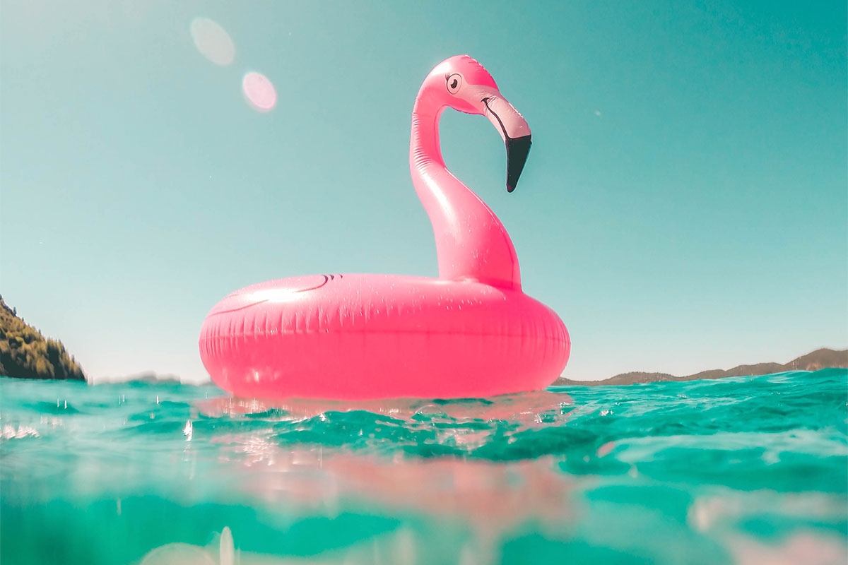 Under the bright sunshine, a pink inflatable flamingo is floating on the sea