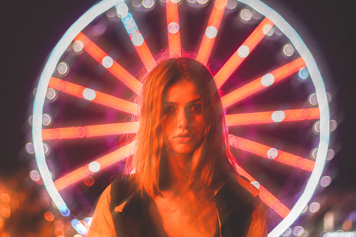 A woman in front of a merry-go-round with blurred background and warm red light illuminating her face