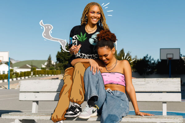 Two joyful women sitting on a white bench, smiling, with trees in the background, basking in the warmth of a sunny day