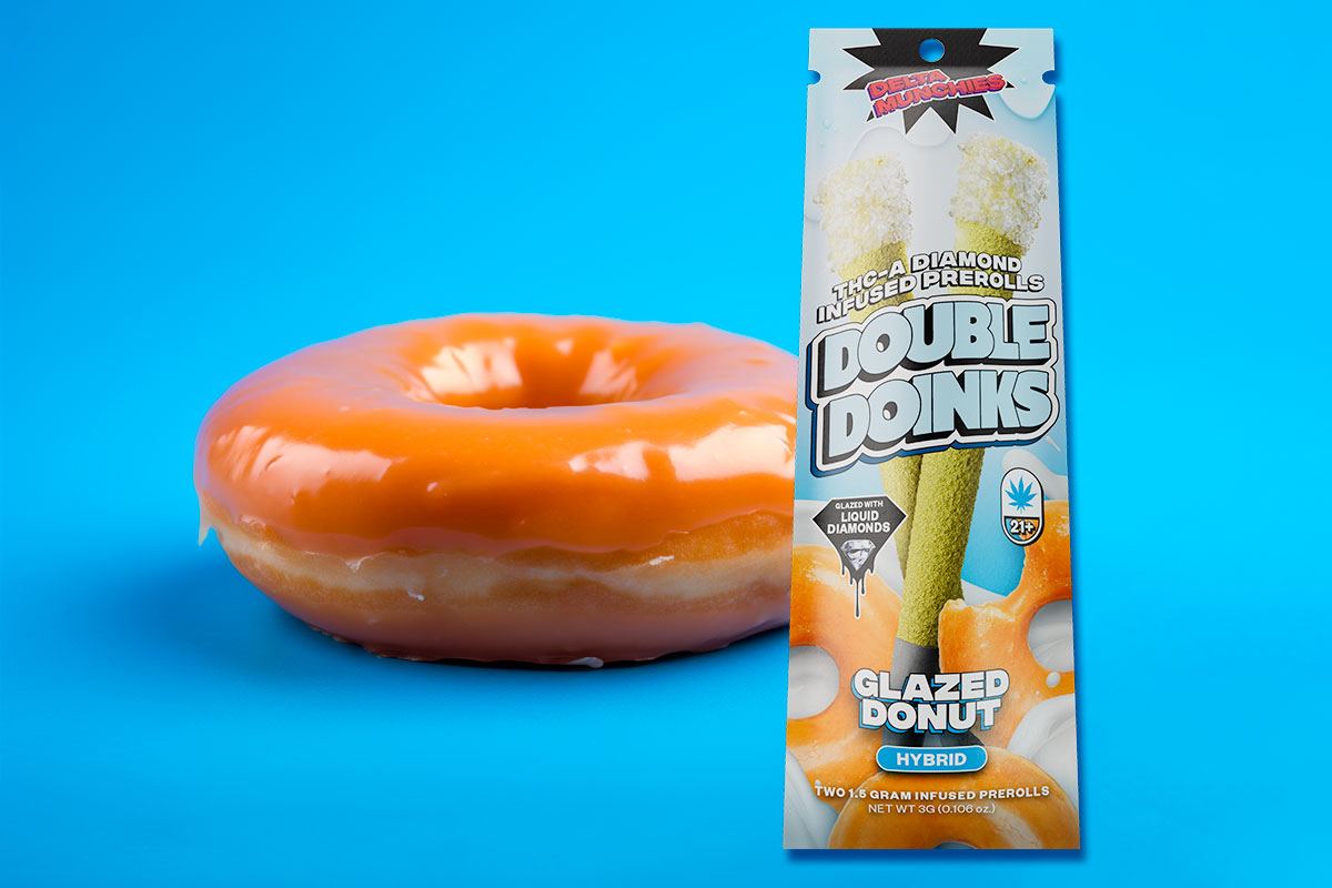Delta Munchies THC-A Diamond Infused Prerolls Double Doinks with Glazed Donut flavor, with a donut placed behind the pack on a blue surface