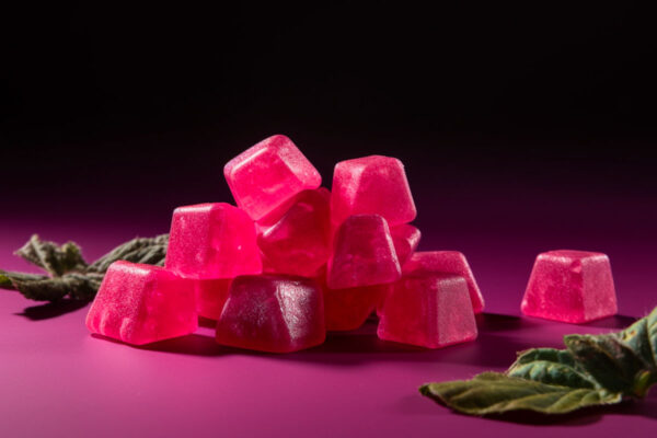 Pink cube gummies on pink surface, with leaves, against a dark background
