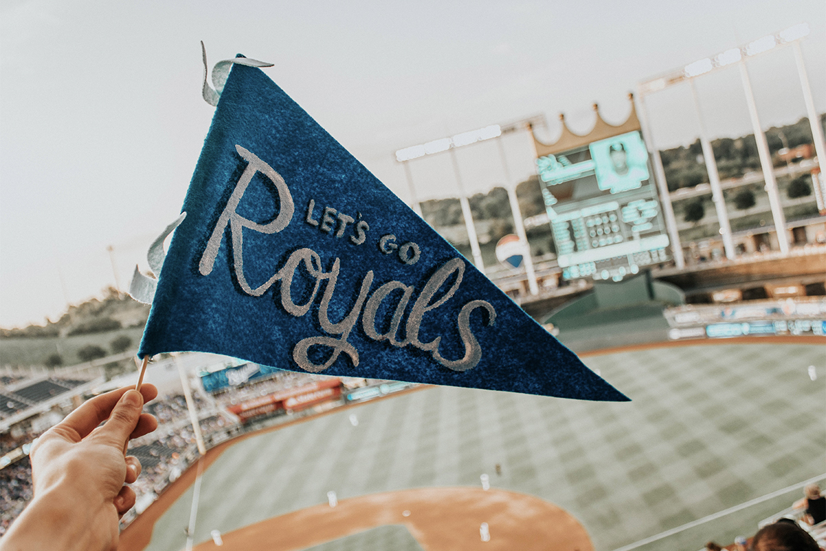 Crowded Kauffman Stadium, enthusiastic man with "Let's Go Royals" flag, vibrant atmosphere during a game in Missouri