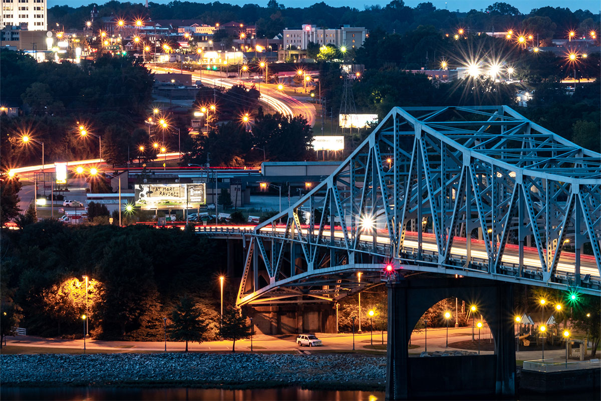 Alabama's O'Neal Bridge at night, aglow with lights, cars on the road, and city buildings