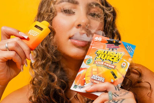 A woman holds a pack of SLUSHY JUICE Mango Gelato flavor in one hand and exhales smoke
