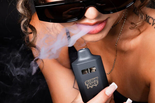 A woman, wearing sunglasses, is holding a black THCP Vape SLUSHY JUICE container and exhaling smoke while smiling with enjoyment