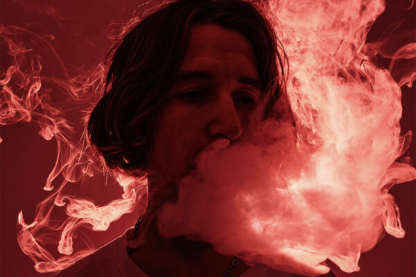 Long-haired man exhaling smoke in a vibrant, reddish glow